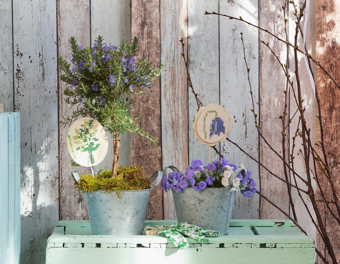 Embroidered plant-pot ornaments in planted zinc pots against vintage wooden wall