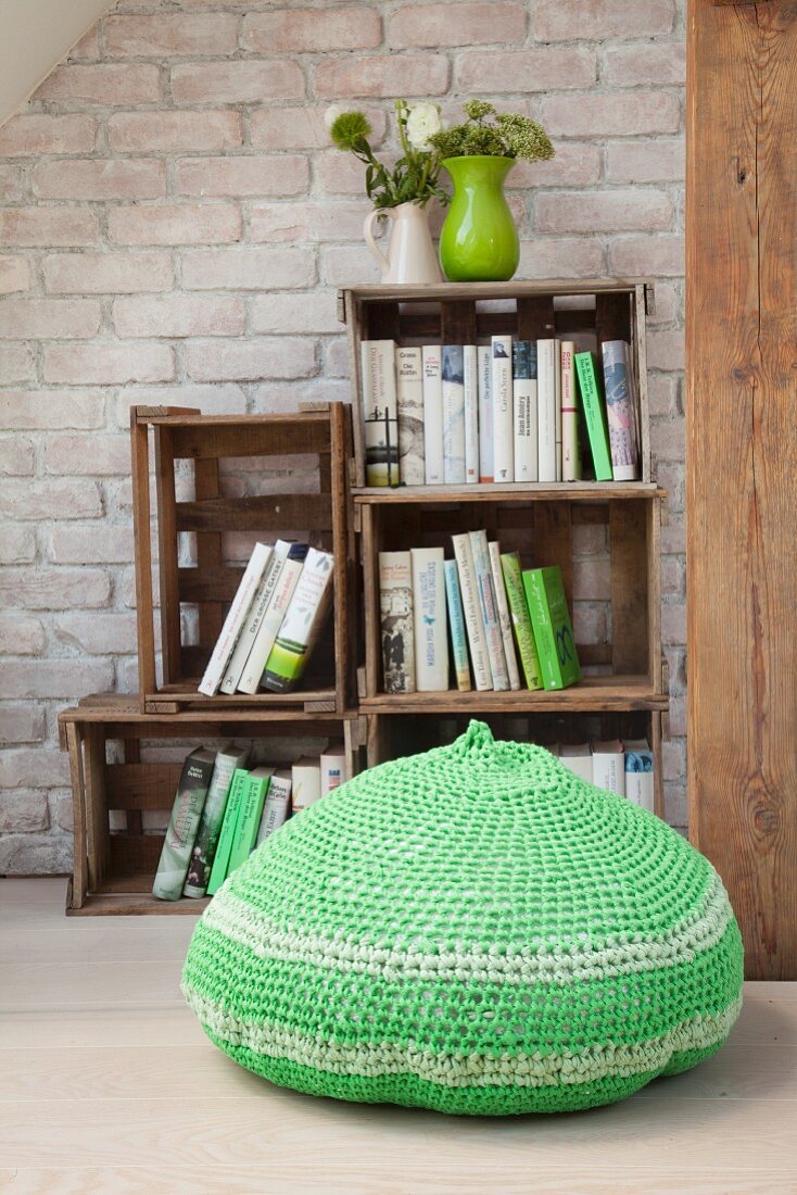 Crocheted, green pouffe in front of bookcase made from stacked wooden crates