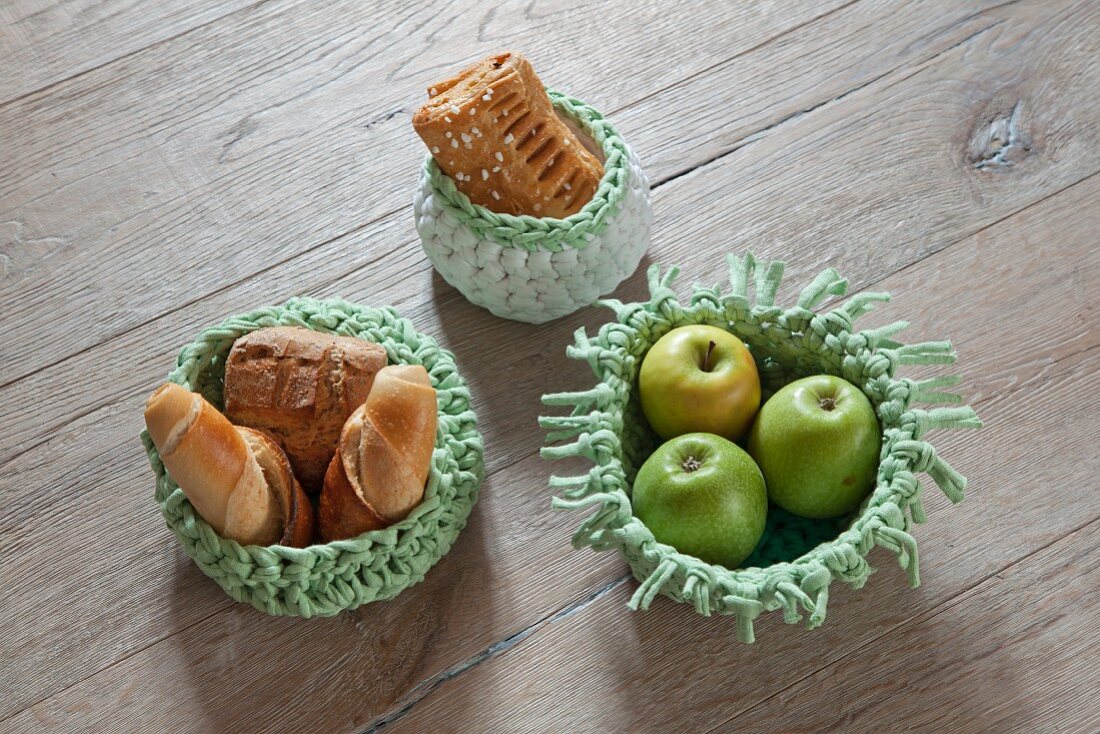 Apples and pastries in crocheted baskets on wooden surface