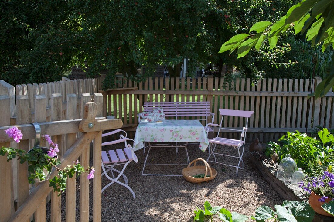 Romantische Sitzplatz vor Lattenzaun und Laubbäumen im Garten
