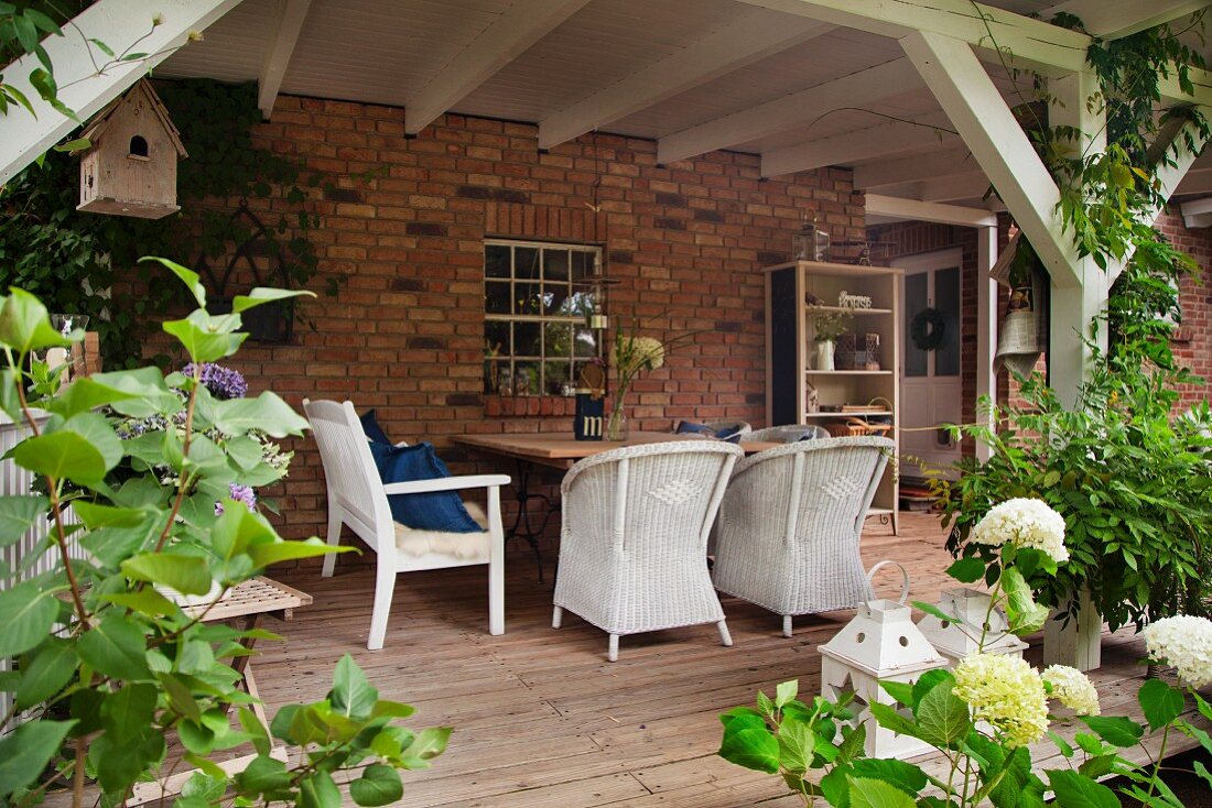 White wicker furniture and garden bench on pleasant wooden terrace against brick façade