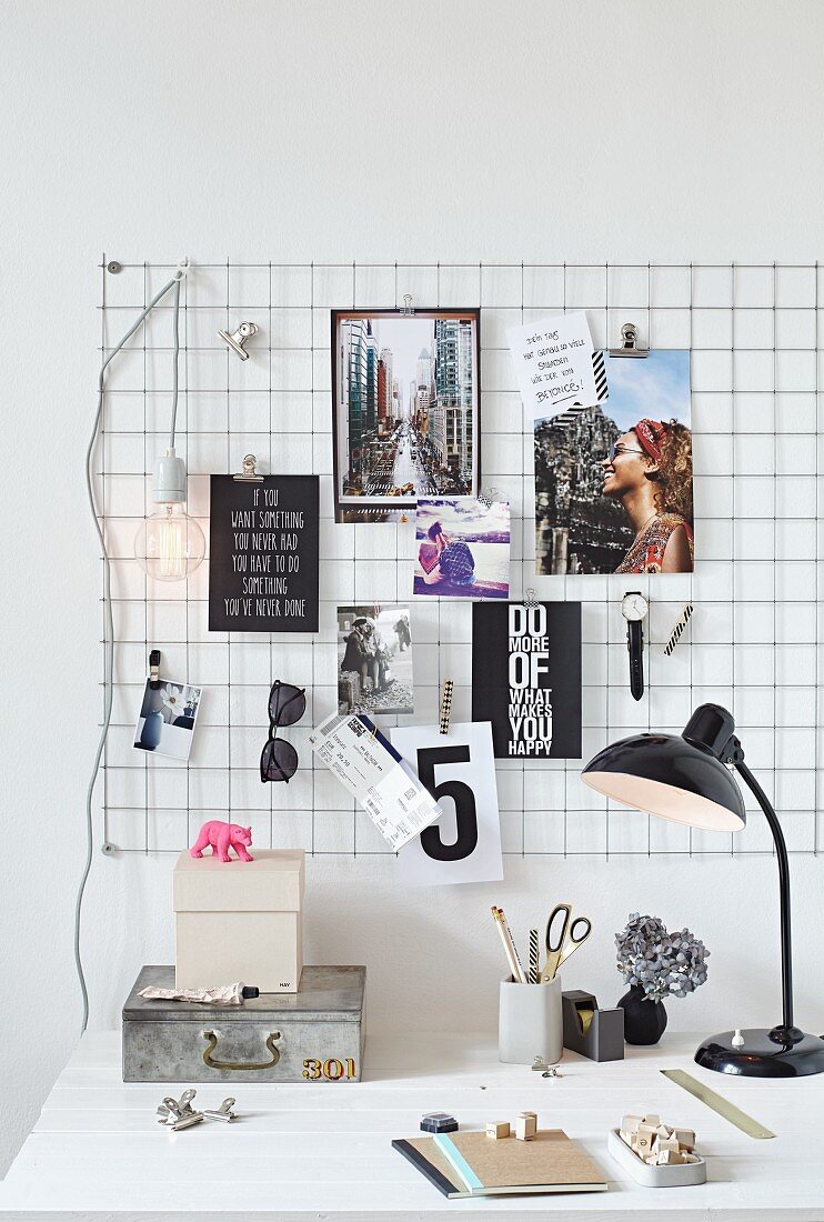 Pinnwand aus Drahtgitter mit Postkarten, Armbanduhr und Sonnenbrille über Schreibtisch