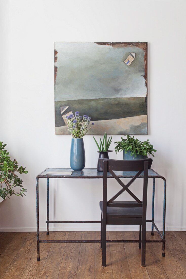 Wooden chair in front of vintage metal table with flowers and green plants in front of modern picture hung on a wall
