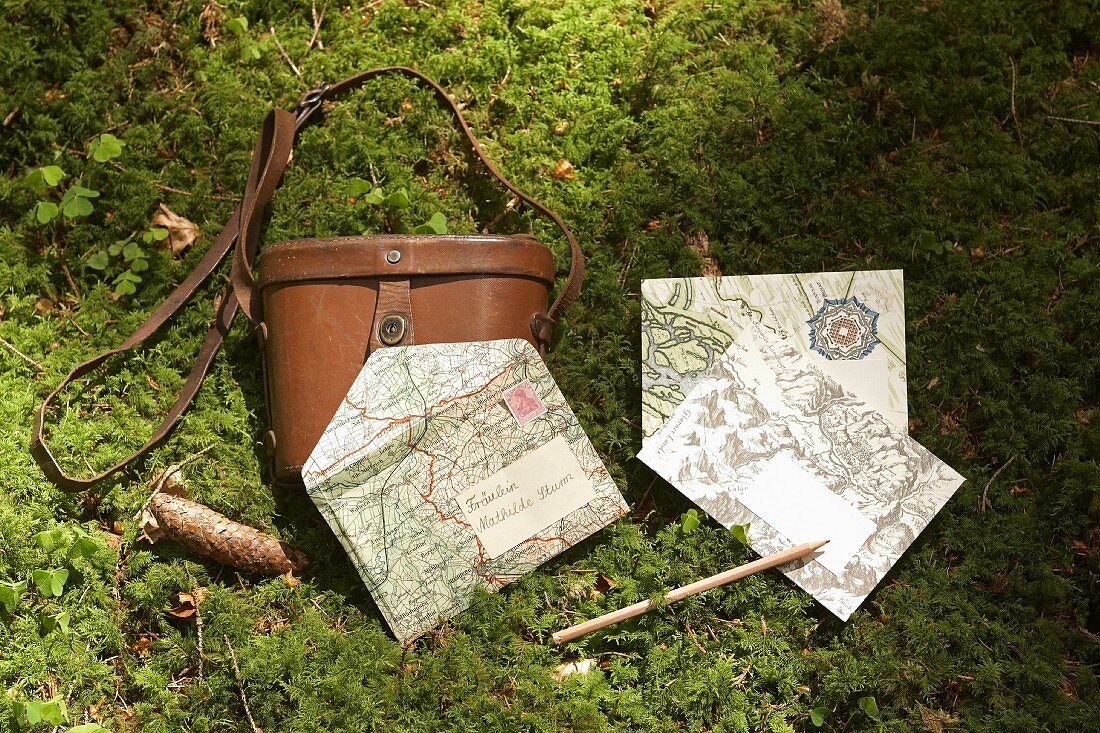 Envelopes made from maps and leather binoculars case on mossy floor