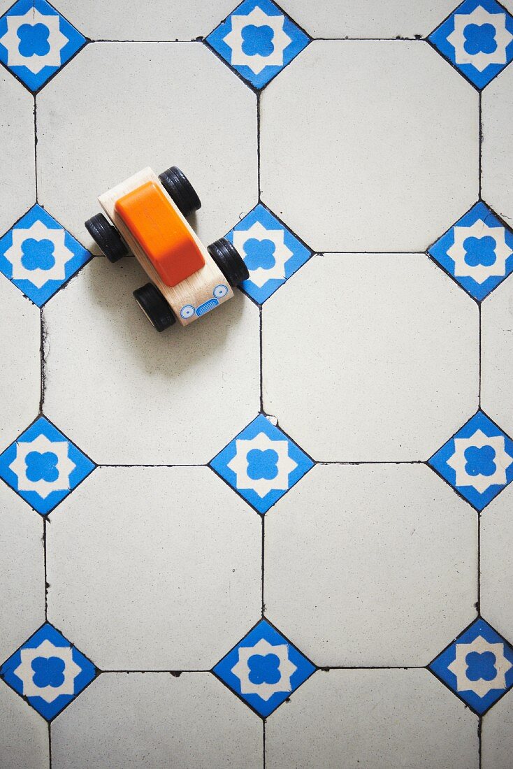 Wooden toy car on traditional white floor tiles with blue ornamental accent tiles