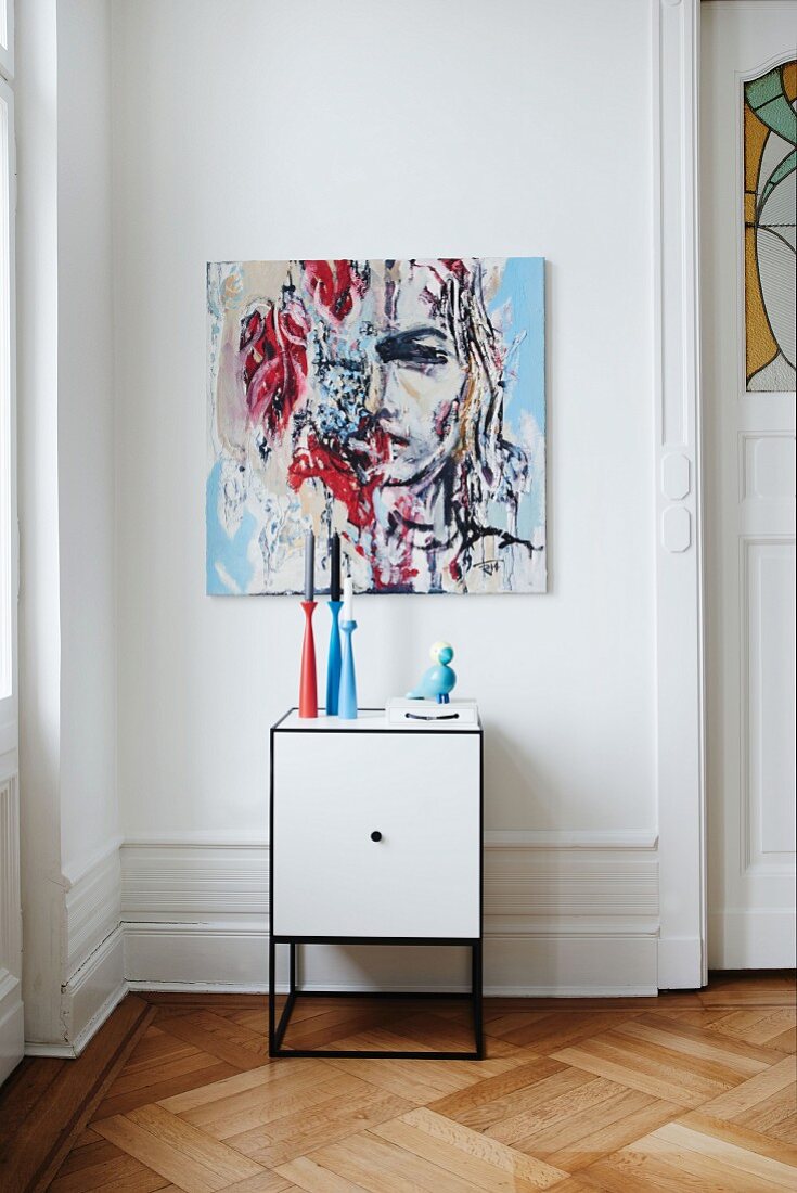 Candlesticks on white cabinet below modern painting