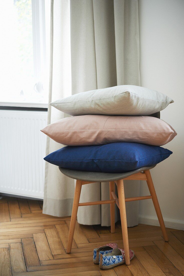 Stacked cushions on retro stool on oak parquet floor
