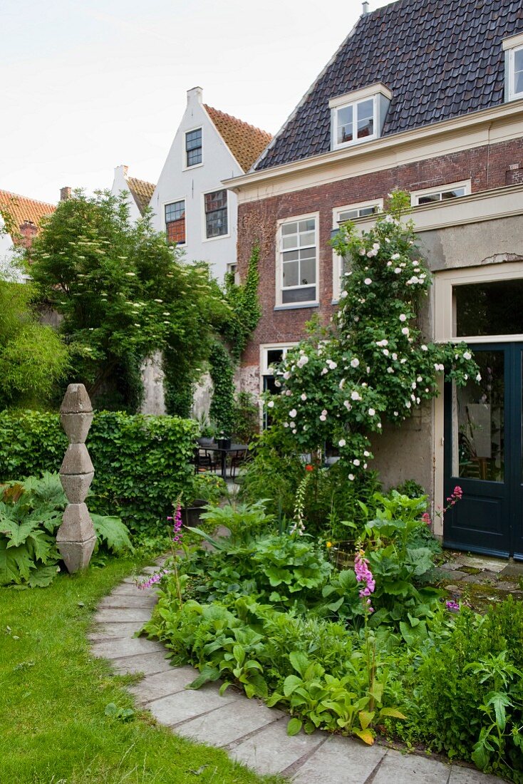 Geschwungener Plattenweg in blühendem grünem Garten einer Villa mit Ziegelfassade