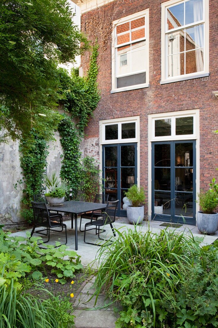 Vom grünen Garten Blick auf schwarze Outdoormöbel und Terrasse vor renovierter Ziegelfassade