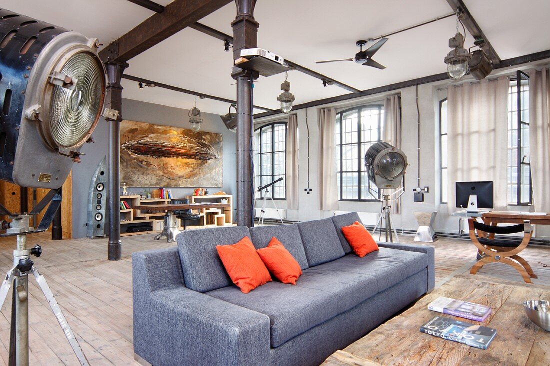 Grey sofa with orange scatter cushions flanked by studio standard lamps in loft apartment with black metal pillars