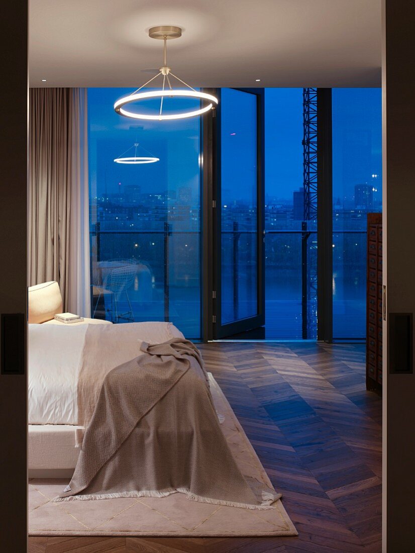 Schlafzimmer mit Blick durch Fensterfront auf Londoner in Abenddämmerung; Retroleuchte mit Leuchtstoffring