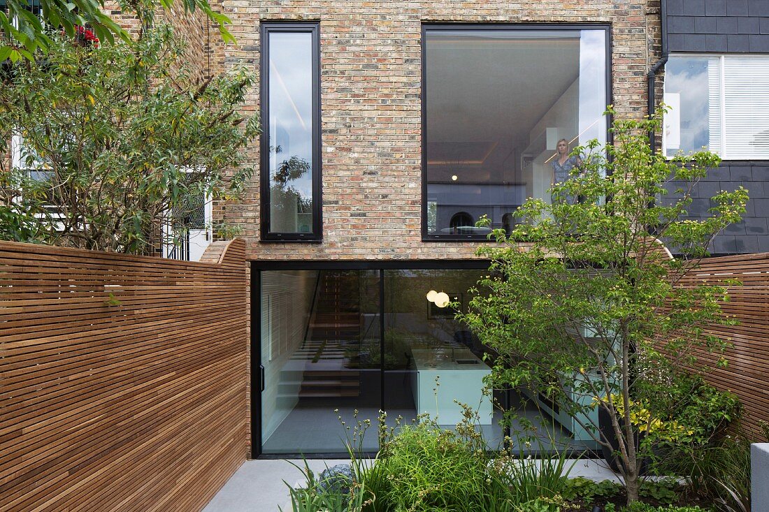 Modern erneuerte Fassade eines historischen Reihenhauses mit Vollverglasung und Garten zwischen Sichtschutzwänden aus Holz