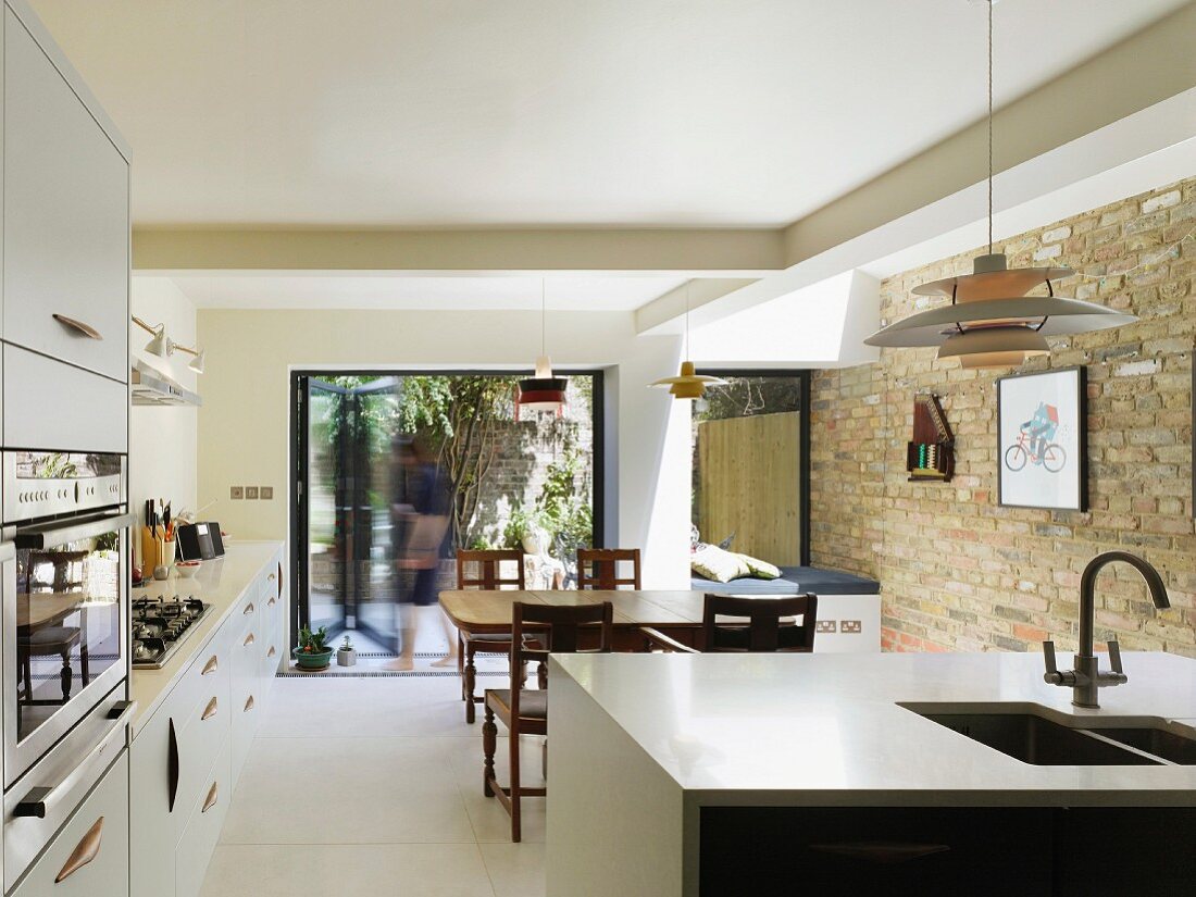 Open-plan, modern kitchen with traditional dining area, old brick wall and view of summer terrace seating area