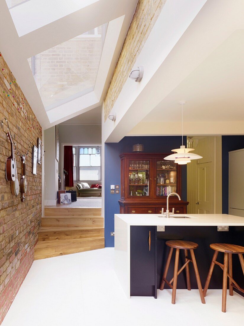 Offene Küche mit weißem Fliesenboden und modernem Oberlichtband zwischen Ziegelwänden, Blick in Wohnbereich