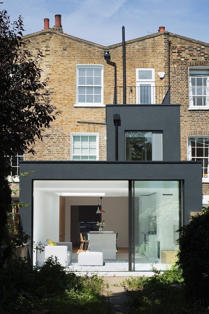 Modern, dark grey extension to Georgian terrace house with open sliding glass wall leading to garden