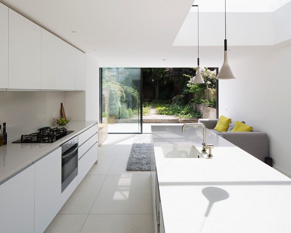 White, designer kitchen with counters, sunlight falling through skylight and view into summery garden