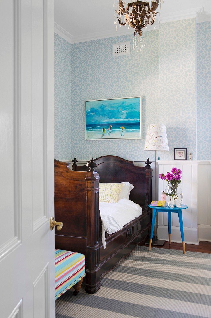 Blick durch offene Zimmertür auf antikes Schlittenbett und blaues Nachttischchen vor holzvertäfelter und tapezierter Wand