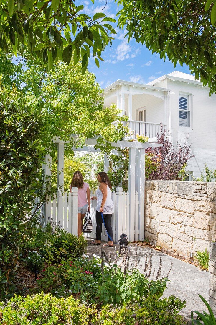 Zwei Frauen mit Hund am weiss lackierten Gartentor vor elegantem Landhaus