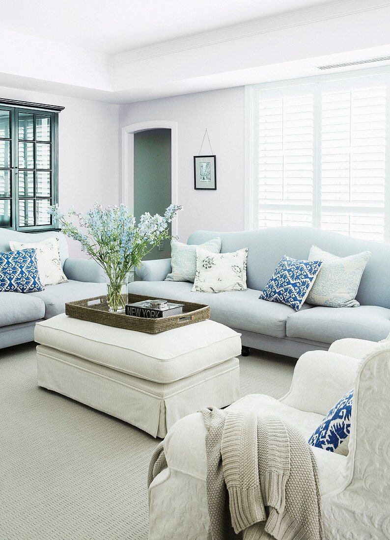 Upholstered table with a bouquet of flowers and elegant sofas in a pastel-colored, rural living room