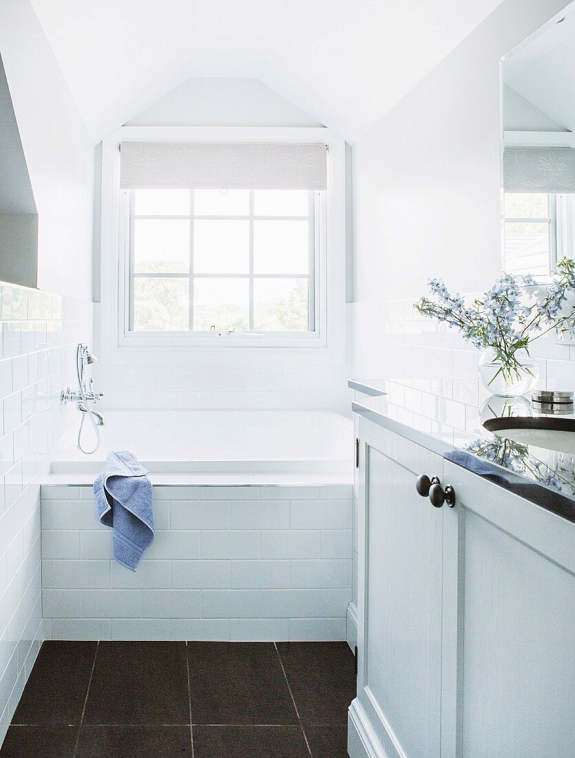 Schmales, weißes Bad mit Waschtischmöbel und eingebauter Badewanne vor Fenster