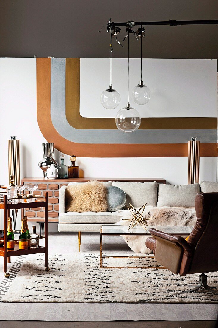 Retro Wohnzimmer, Pendelleuchten mit Glaskugel über Couchtisch und Ledersessel, an Wand Streifendekor in Metalloptik