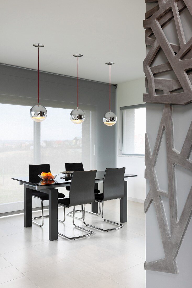 Black dining set on white, tiled floor below shiny, silver pendant lamps in designer interior