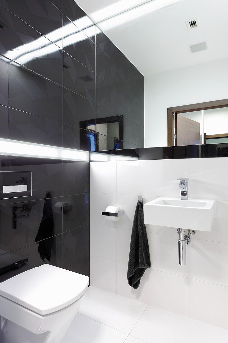 Designerbad mit weißen Bodenfliesen und schwarzen Wandfliesen, Spiegelwand über dem Waschbecken