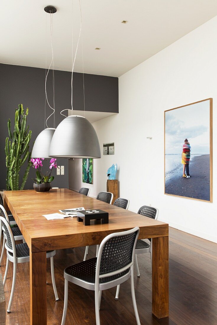 Chairs around solid wooden table below grey pendant lamps