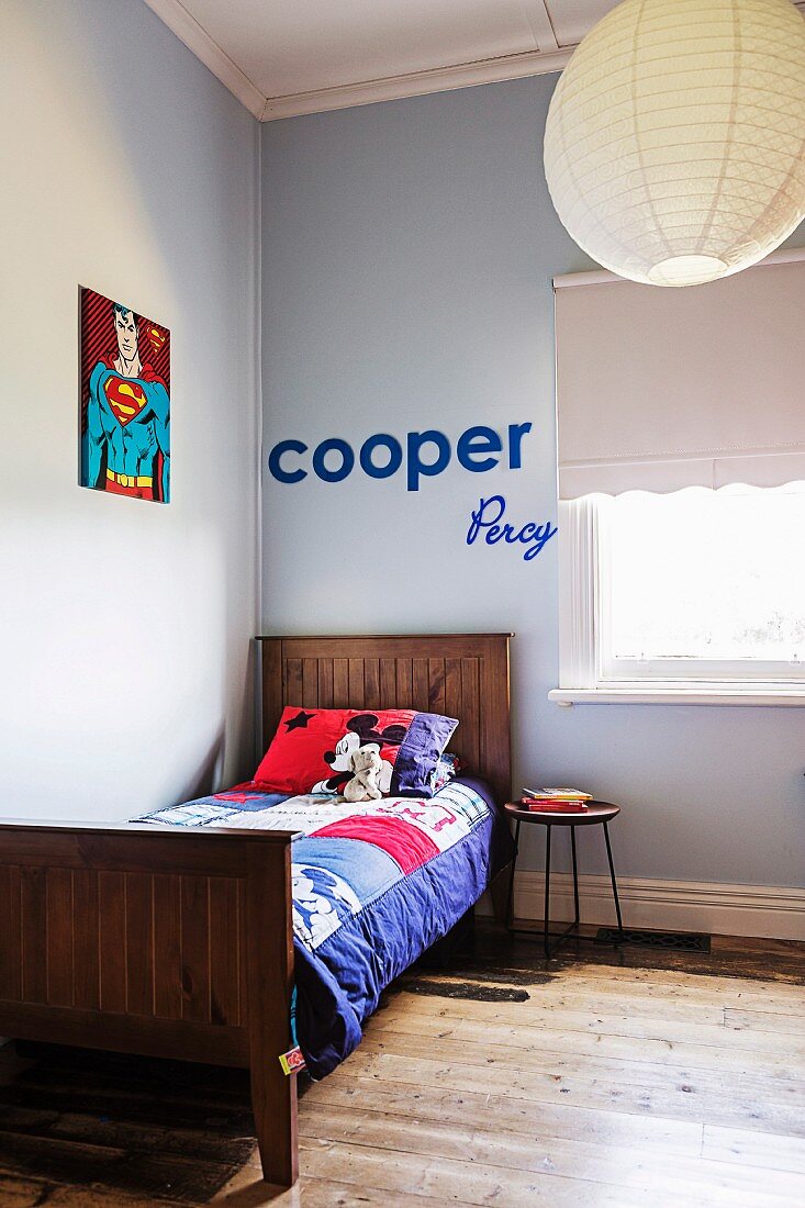 Colorful patchwork blanket on wooden bed in light blue room corner, on wall 'Superman' picture and decorative letters