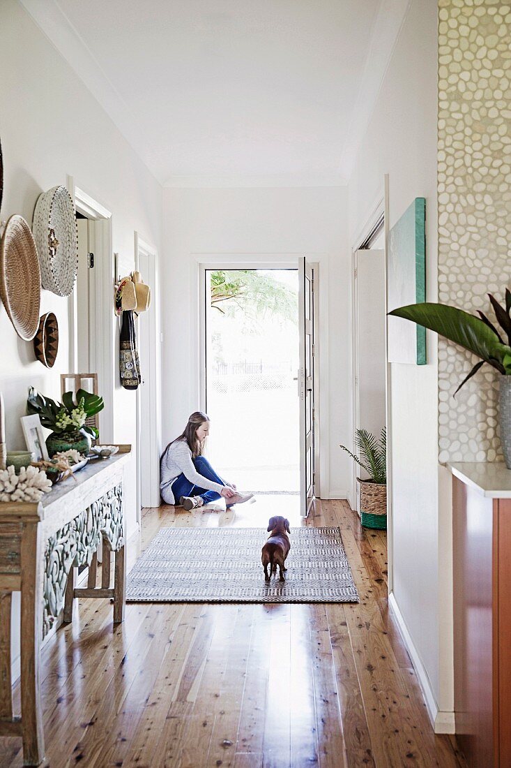 Entrance area with shiny floorboards, in the background girl in front of an open door with a dachshund on a carpet runner