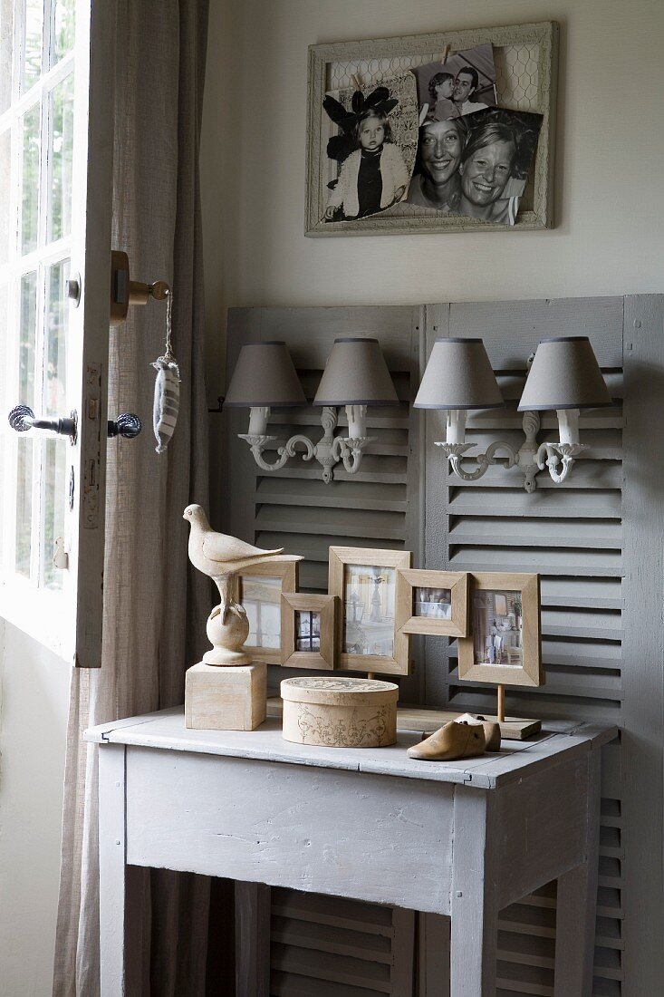 Grey wooden table below sconce lamps hung on panelling made from old window shutters