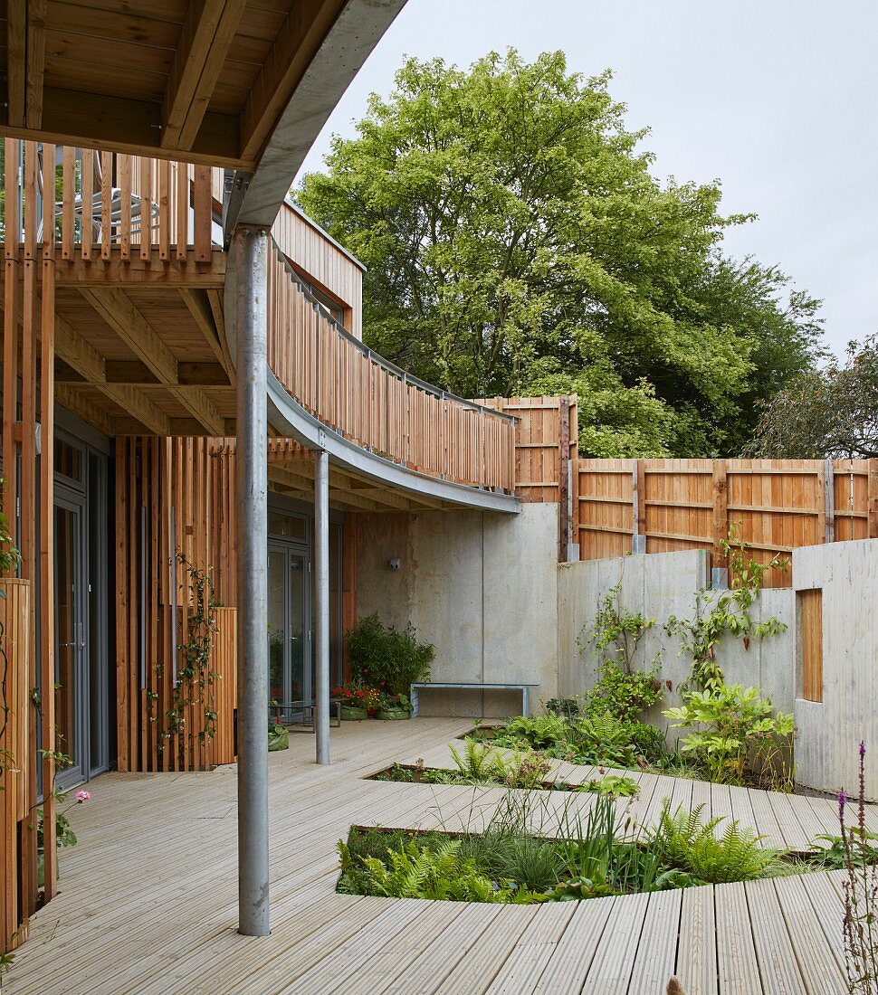 Modernes gemeinschaftliches Ökohaus mit umlaufendem gebogenem Balkon und Holzterrasse mit ausgeschnittenen Pflanzbeeten