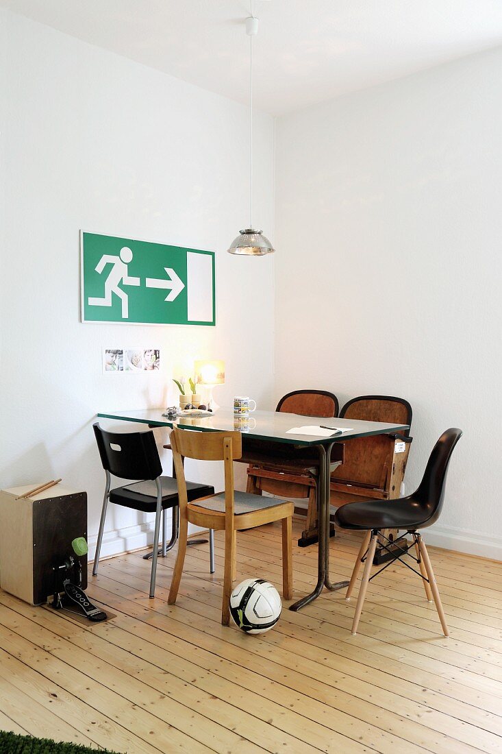 Schlichter Essplatz mit verschiedenen Stühlen in minimalistischer Zimmerecke, vor Schild an Wand, gepflegter, alter Dielenboden