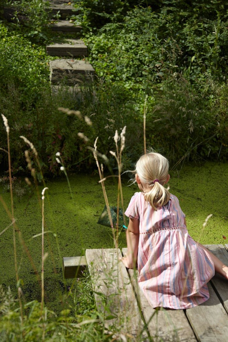 Blonde girl fishing from wooden jetty next to garden pond