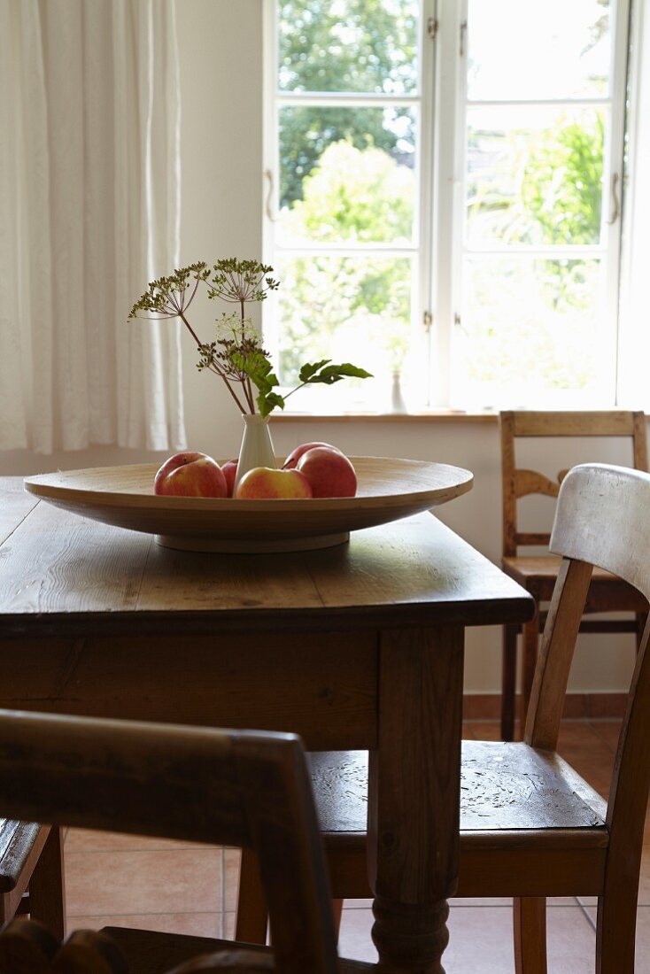 Fruit bowl and vase of flowers on wooden table in front of window