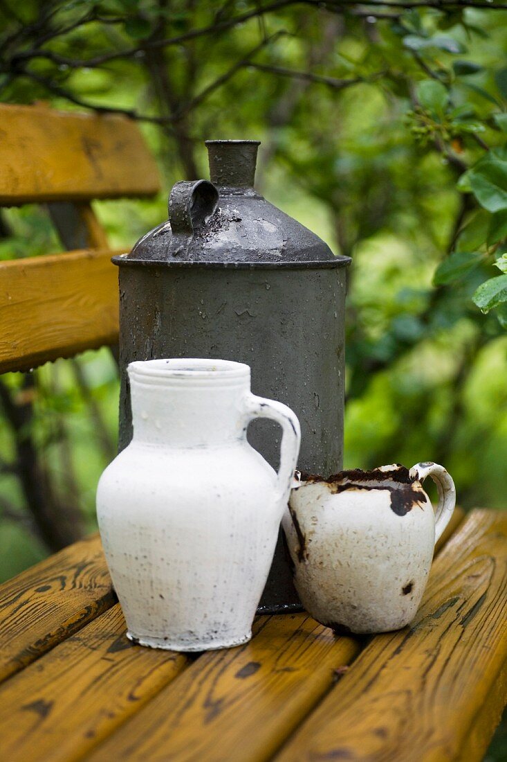 Vintage-style, still-life arrangement of white jugs and canister on wooden bench in garden
