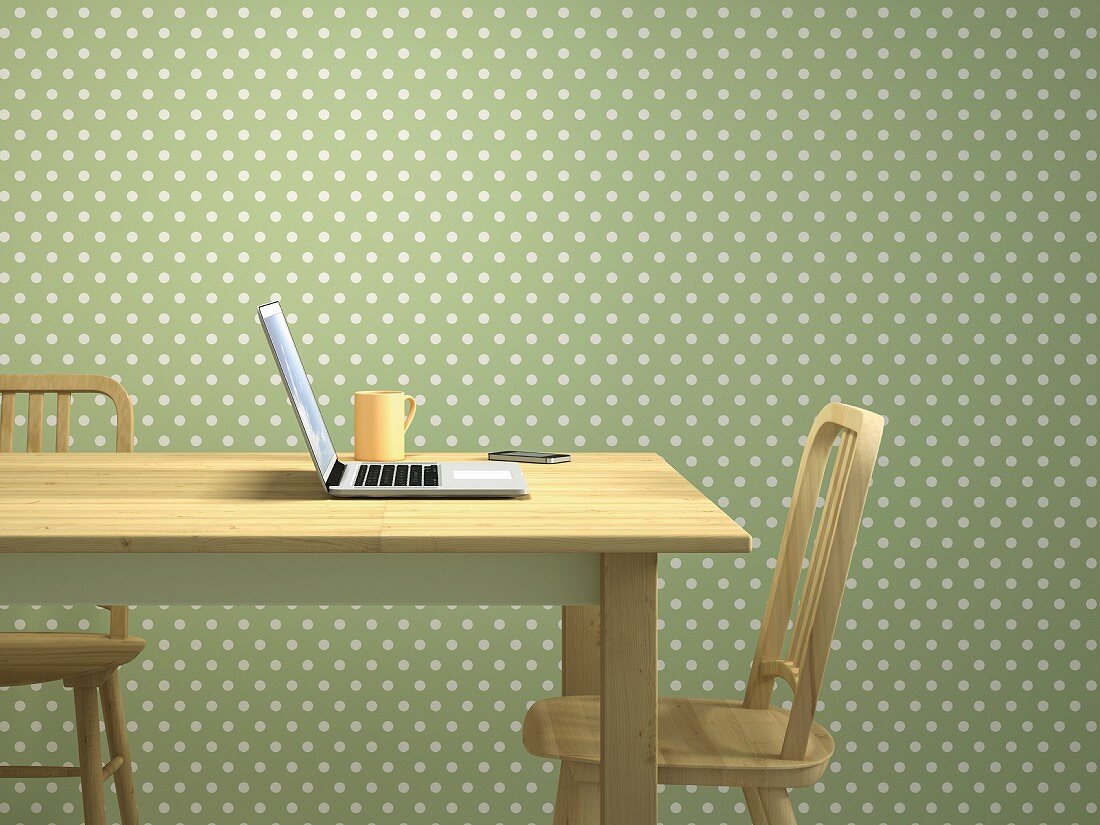 Laptop & mobile phone on wooden table in front of green and white polka-dot wallpaper