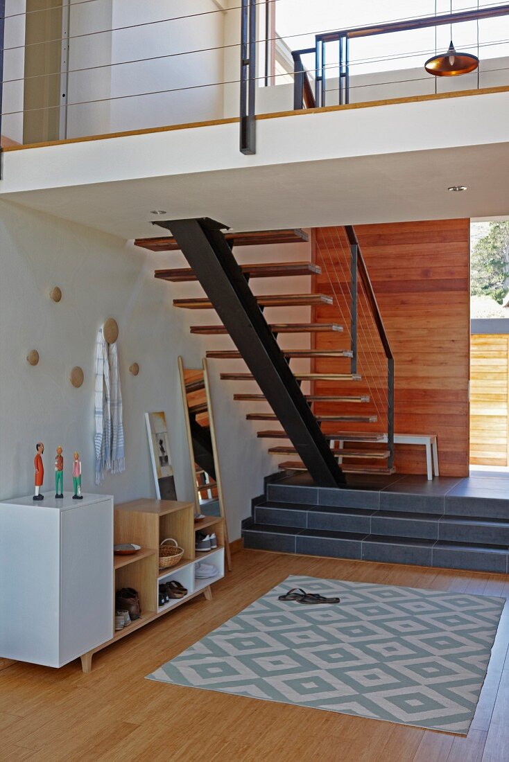 Gemusterter Teppich auf Holzboden, vor Podest und Treppenaufgang, seitlich an Wand Garderobenmöbel