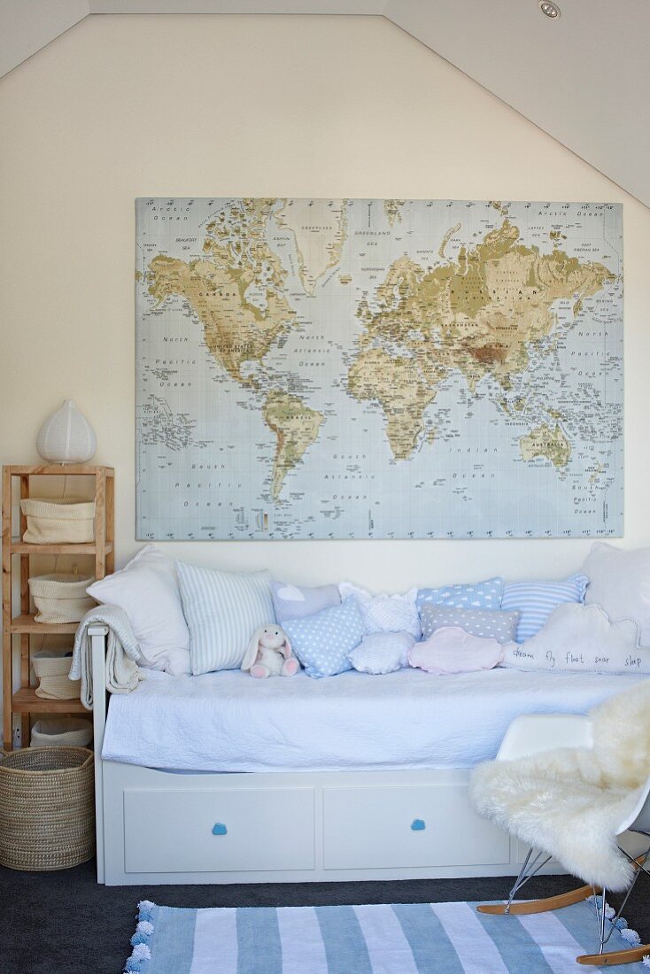 Pale blue cushions on child's bed with integrated drawers below world map hung on gable-end wall of attic room