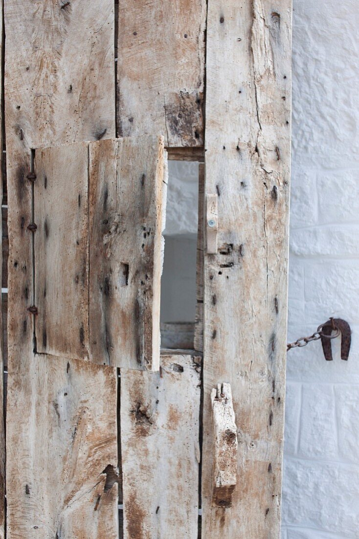 Alte Haustür aus Holzbrettern mit kleiner Klappe zum Öffnen