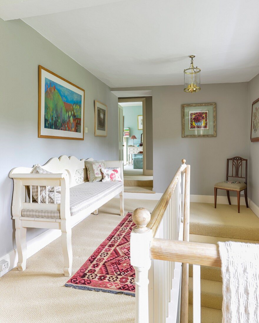 Hellgrau getönter Flur mit traditioneller, weißer Sitzbank am Treppenabgang mit Geländer