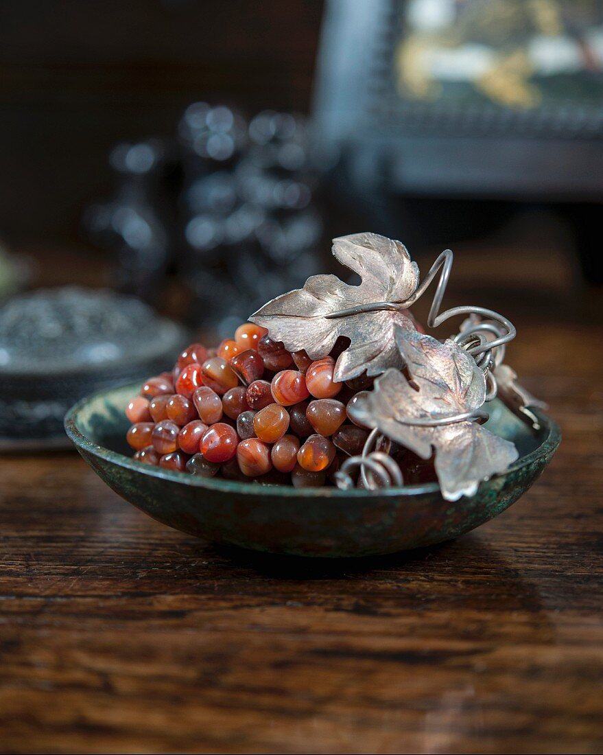 Schale mit künstlerischer Weintrauben aus Edelsteinen und kunsthandwerklich gefertigten Silberblättern auf Holztisch