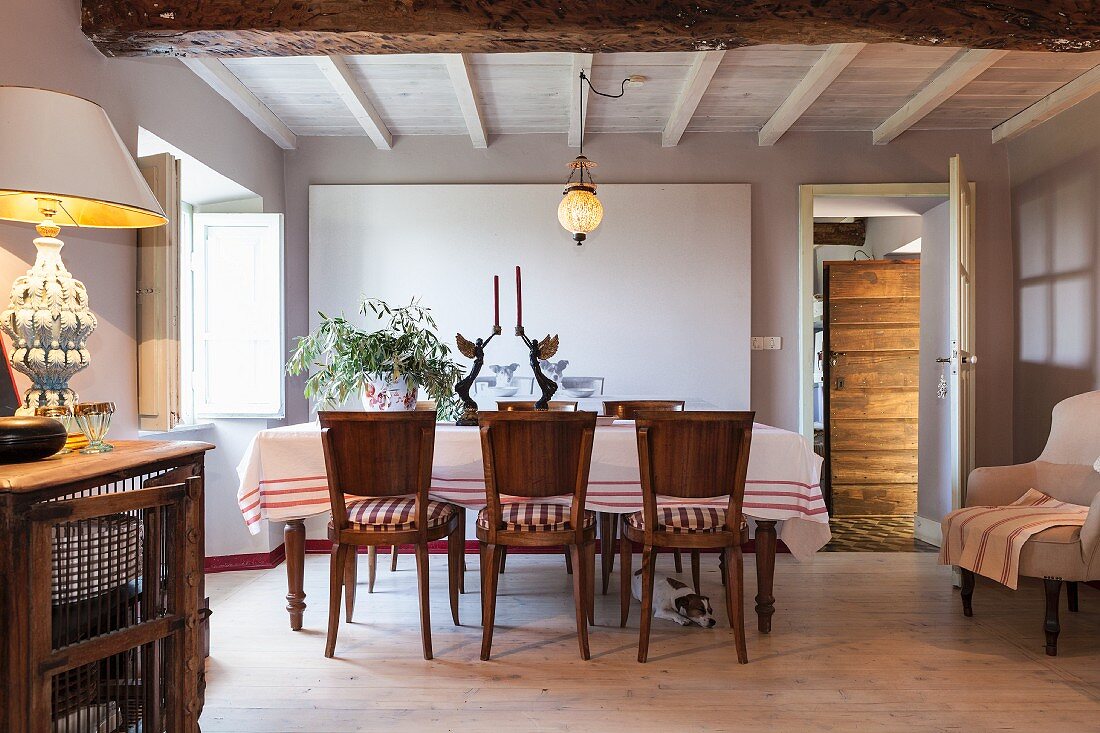 Esstisch mit Tischdecke und Holzstühlen in mediterranem Esszimmer unter weißer Holzbalkendecke