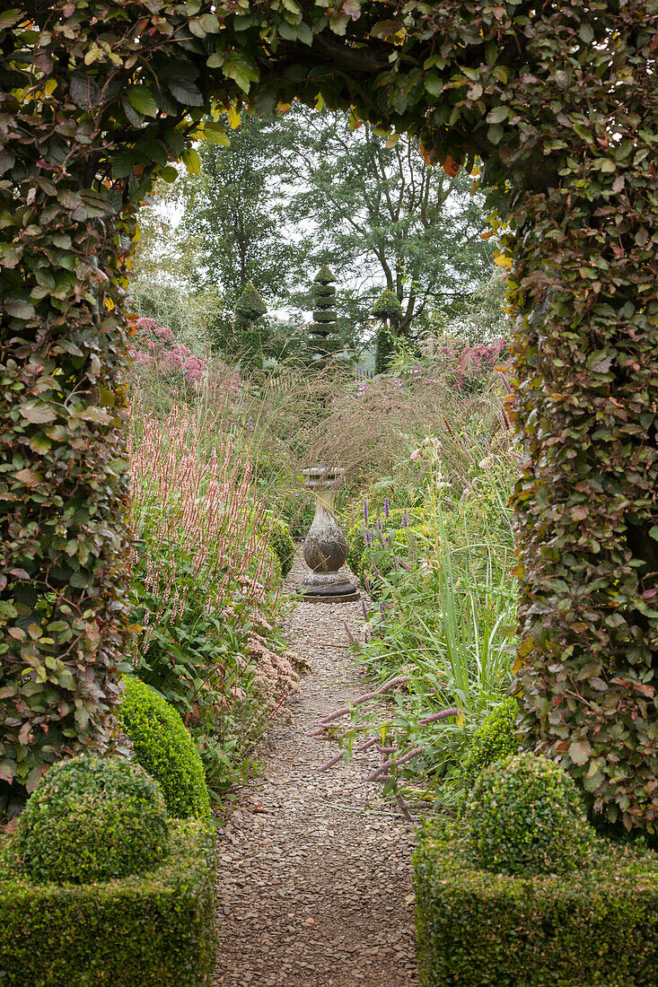 Blick durch eine Hecke mit Torbogen in einen Formgarten