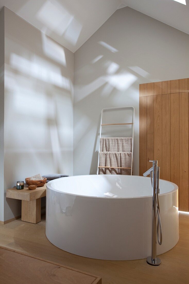 Free-standing round bathtub with floor-mounted taps in minimalist attic bathroom