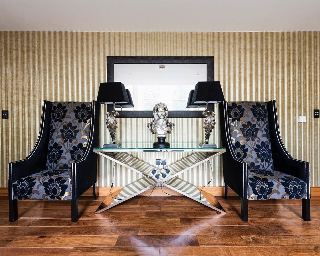 Luxuriöse Armlehnsessel mit gemustertem Bezug neben extravagantem Tisch mit Büste und Tischleuchten