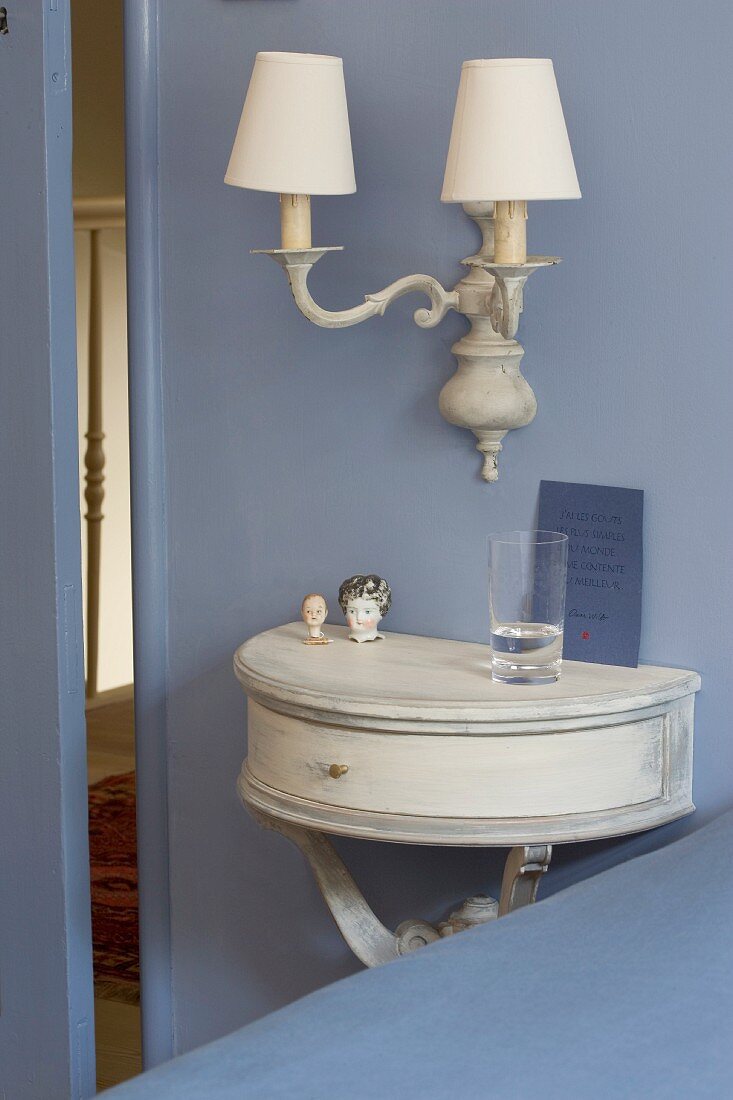 Semicircular console table below sconce lamp with lampshades on pastel-blue wall