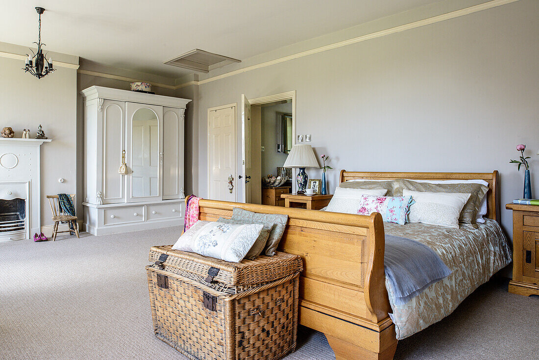 Wicker trunk at foot of wooden bed in classic bedroom