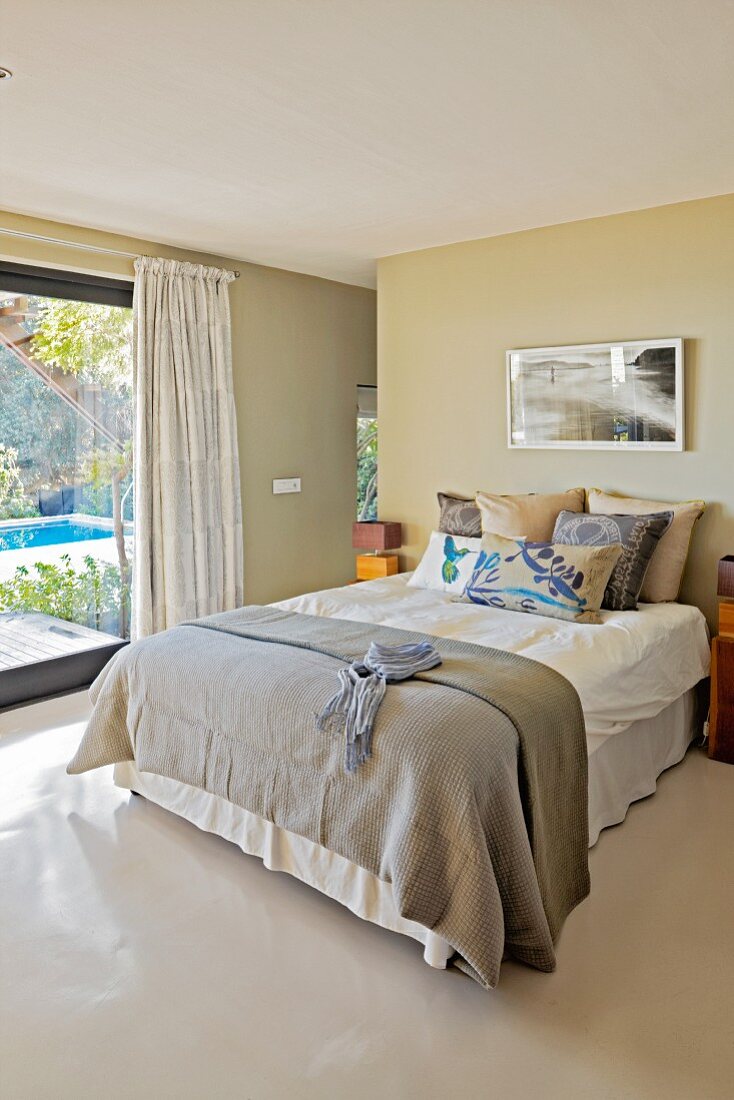 Graue Tagesdecke auf Doppelbett neben Terrassentür in modernem Schlafzimmer mit hellgrauem Epoxidharzboden