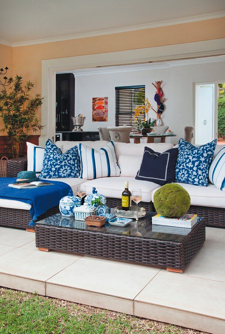 Dunkle Rattan Outdoormöbel, Bodentisch und Sofa mit gemusterten Kissen in Blau und Weiß auf gefliester Wohnterrasse
